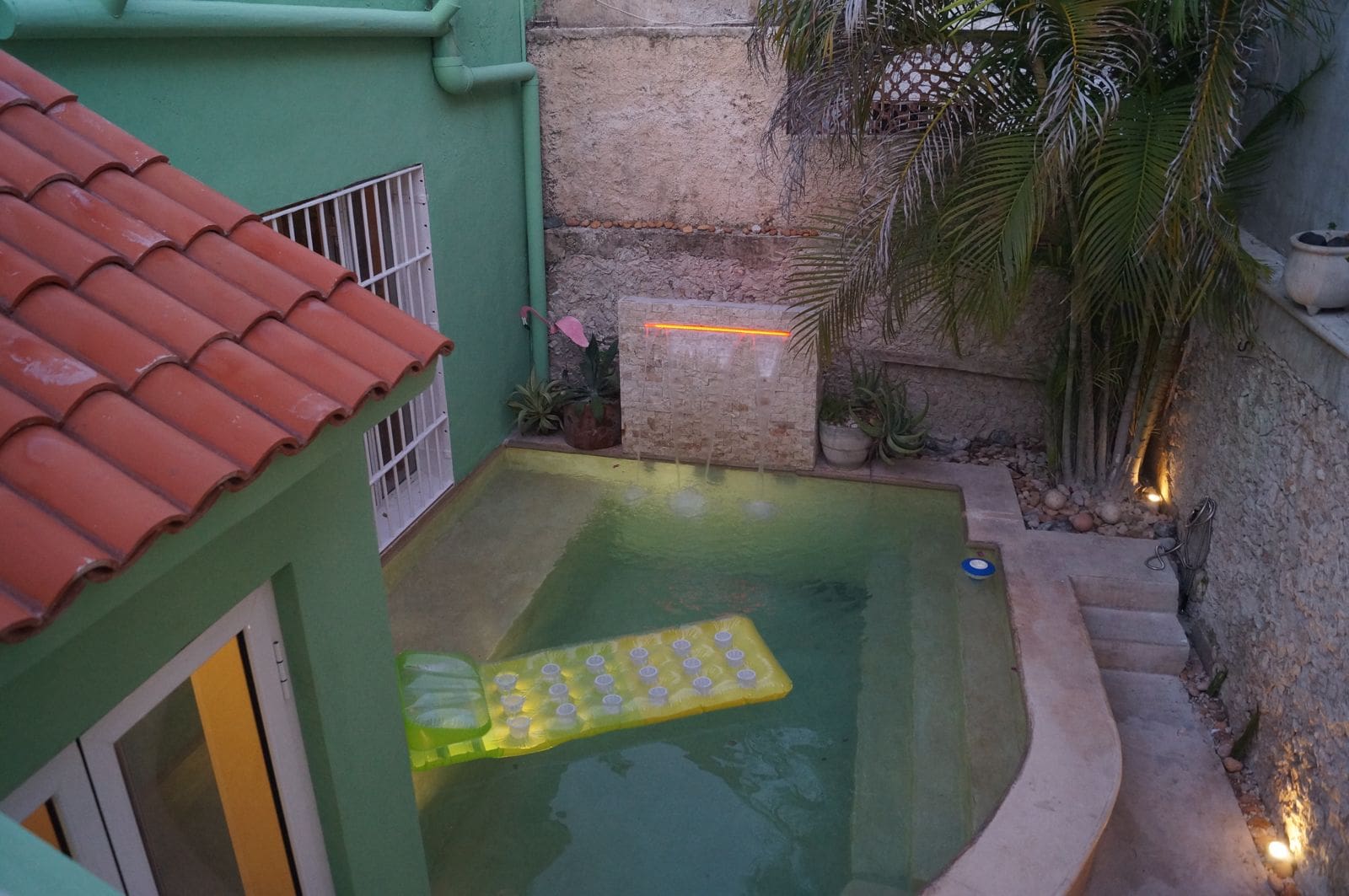Small backyard pool with a floating mattress and green walls.