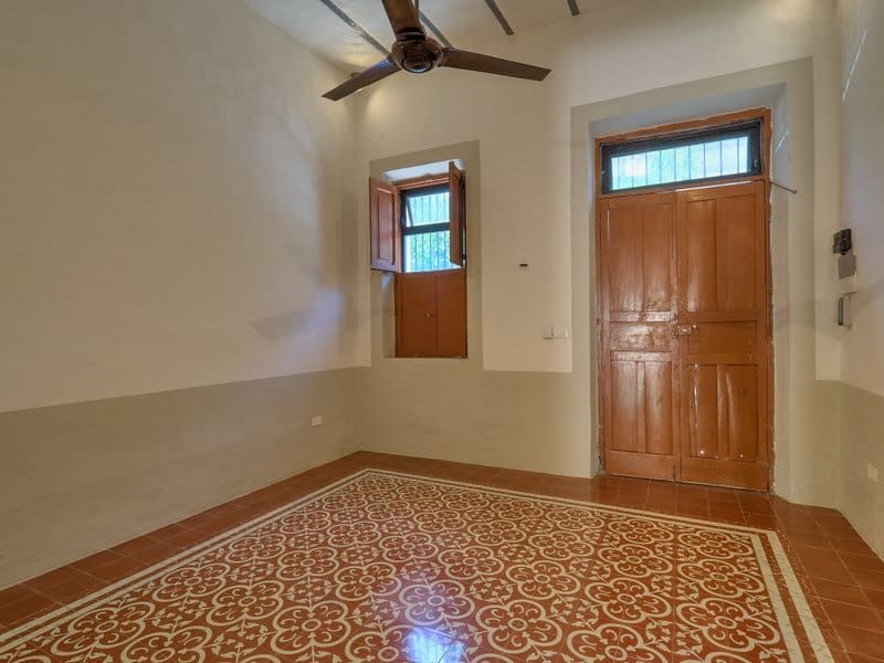 Empty room with wooden door, window, and patterned tile floor.