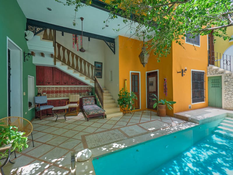 Cozy outdoor patio with stairs, vibrant orange walls, and a serene pool under leafy greenery.
