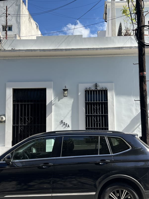 Black car parked in front of a white building with barred windows.