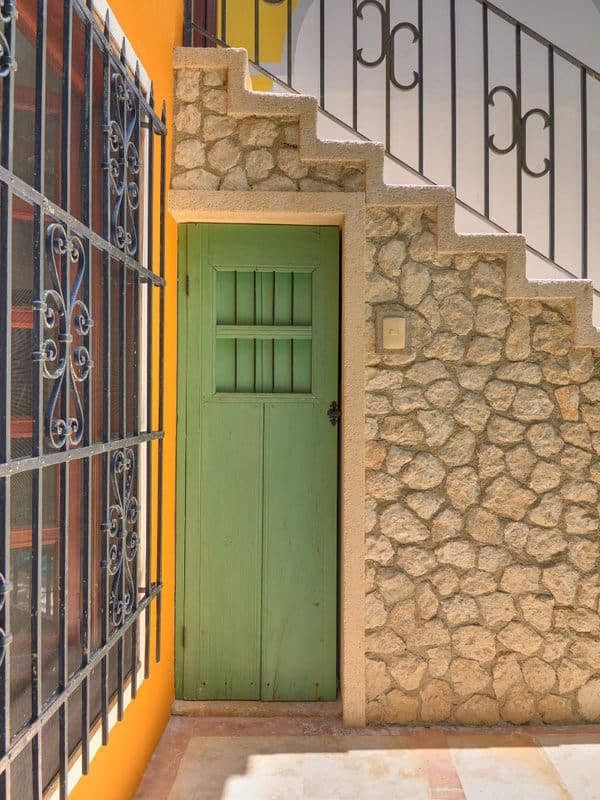 Green door under a stone-textured staircase with metal railing.