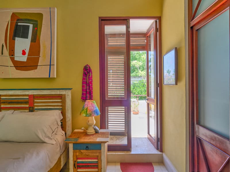 Sunny bedroom with open door leading to a balcony and garden view.