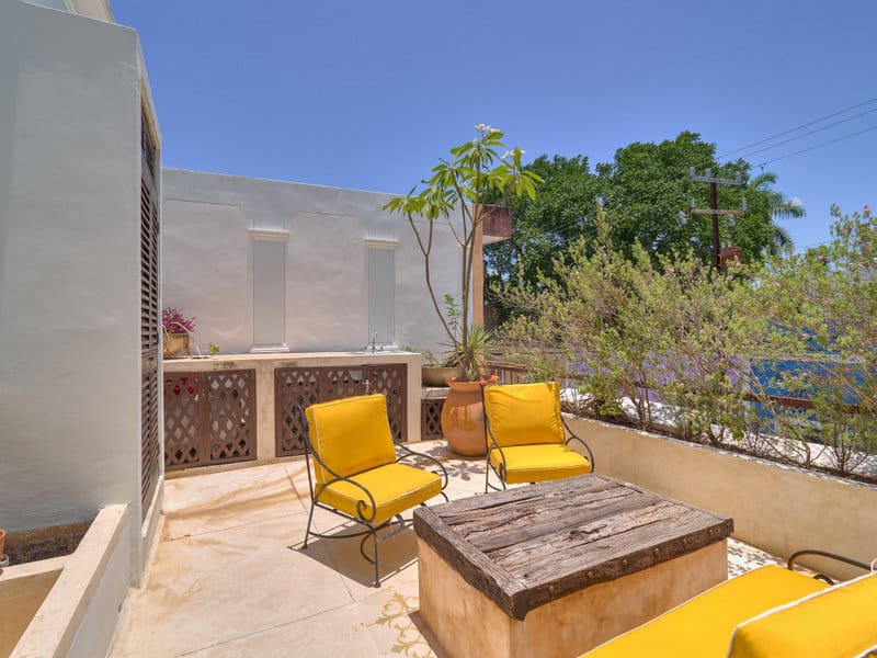 Sunny outdoor patio with yellow chairs and a fire pit table under clear skies.