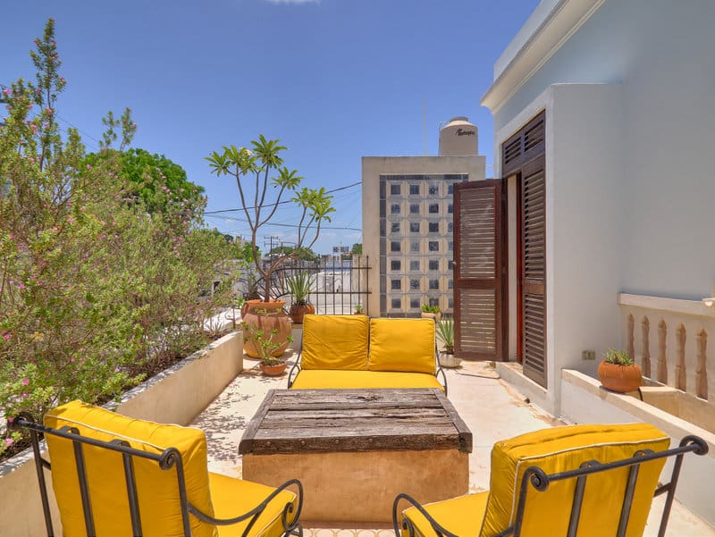 Sunny outdoor patio with yellow cushioned seating and a city view.