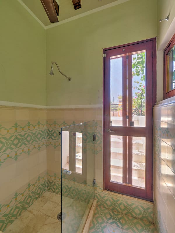 Sunlit bathroom with glass shower door and decorative tile walls.