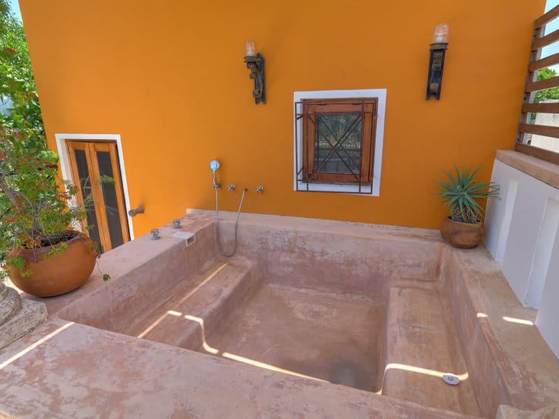 Empty stone pool against a vibrant orange wall with window and sconces.