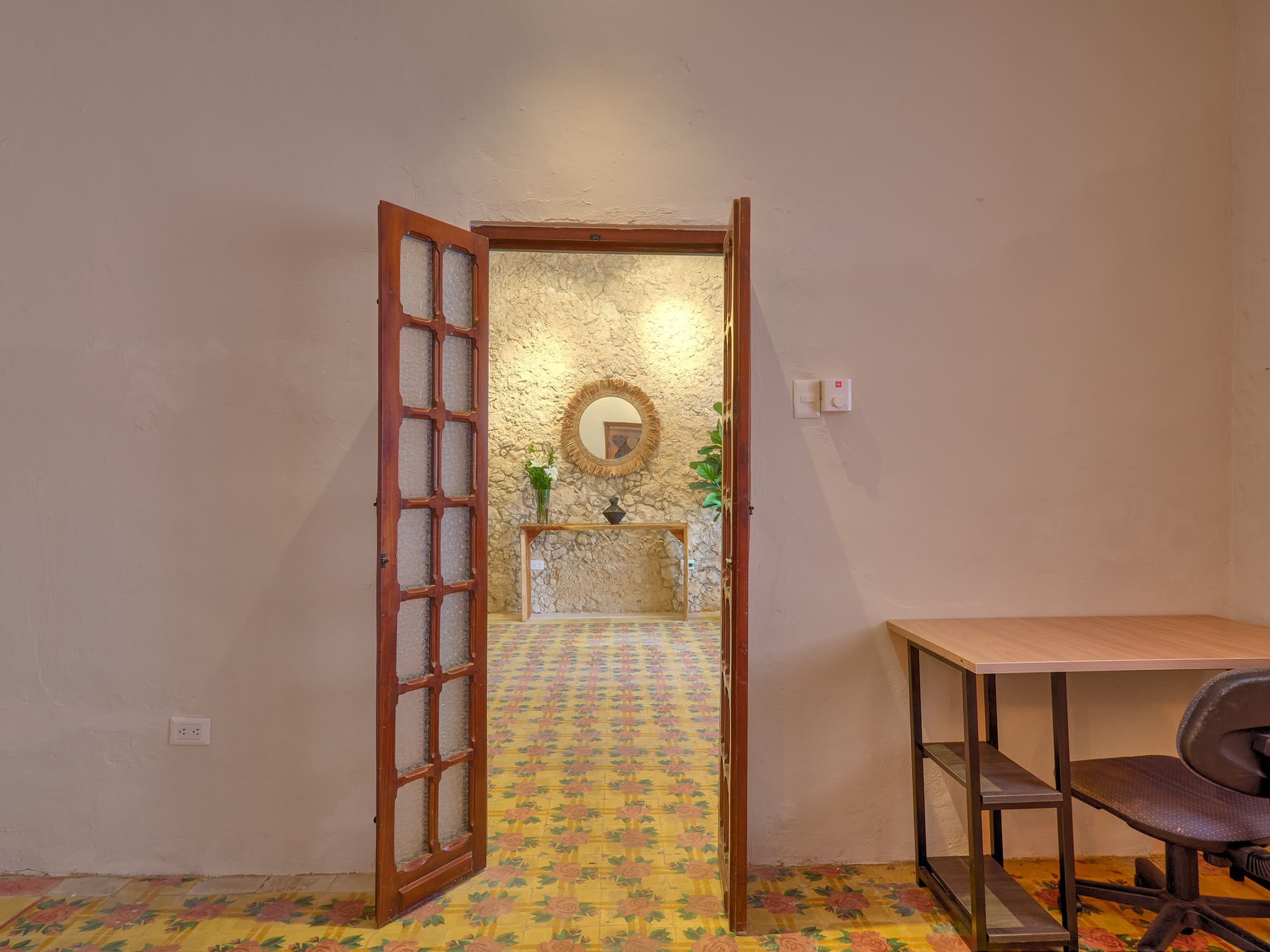 Open wooden door revealing a bright, decorated room with plants and a round mirror.
