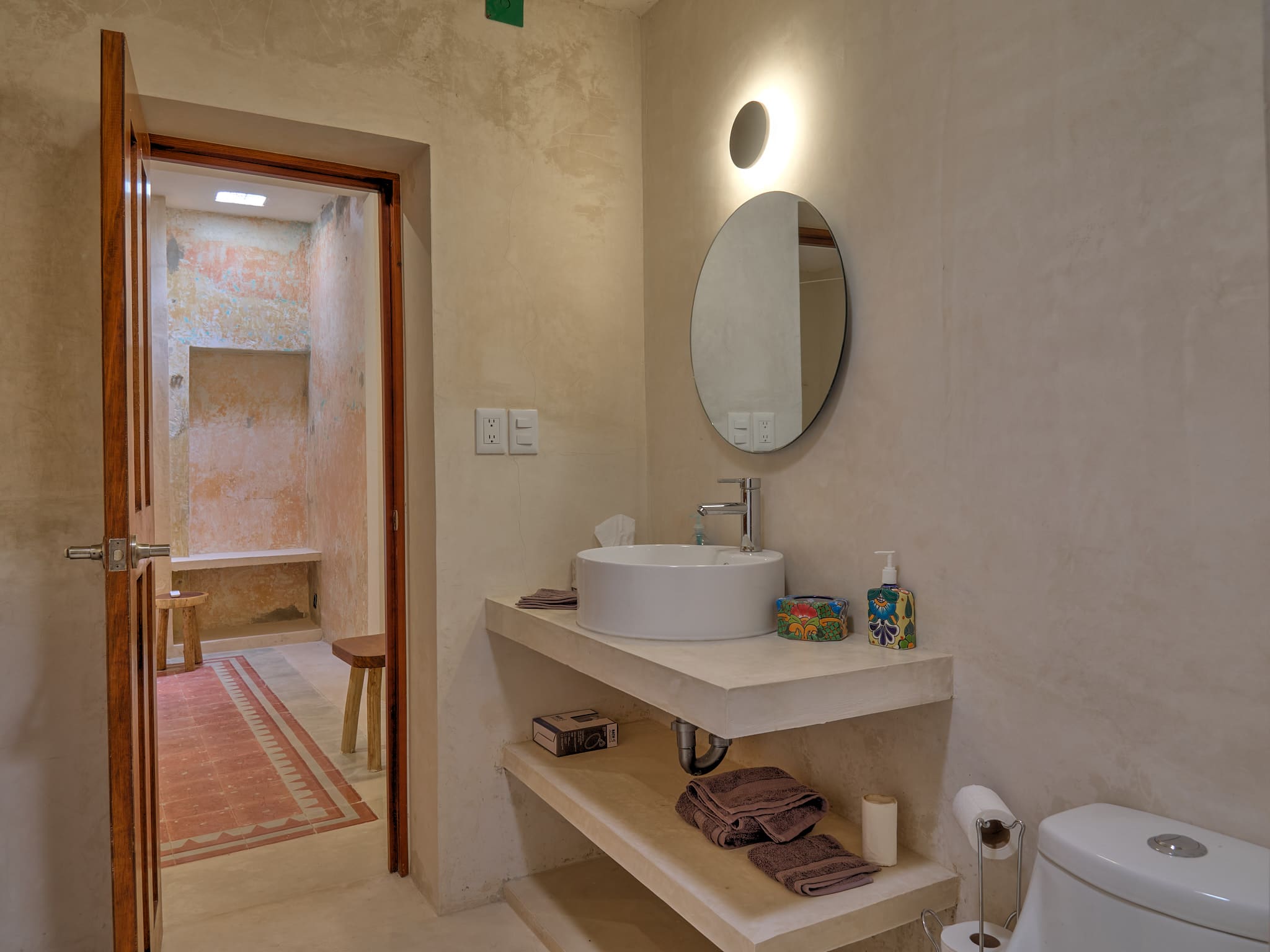 Modern bathroom with a round mirror and floating wooden shelves.