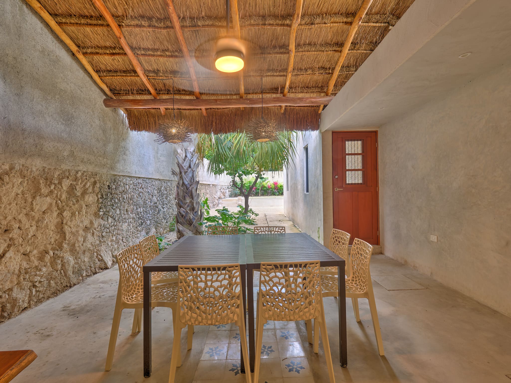 Rustic outdoor dining area with wooden table and chairs under a thatched roof.
