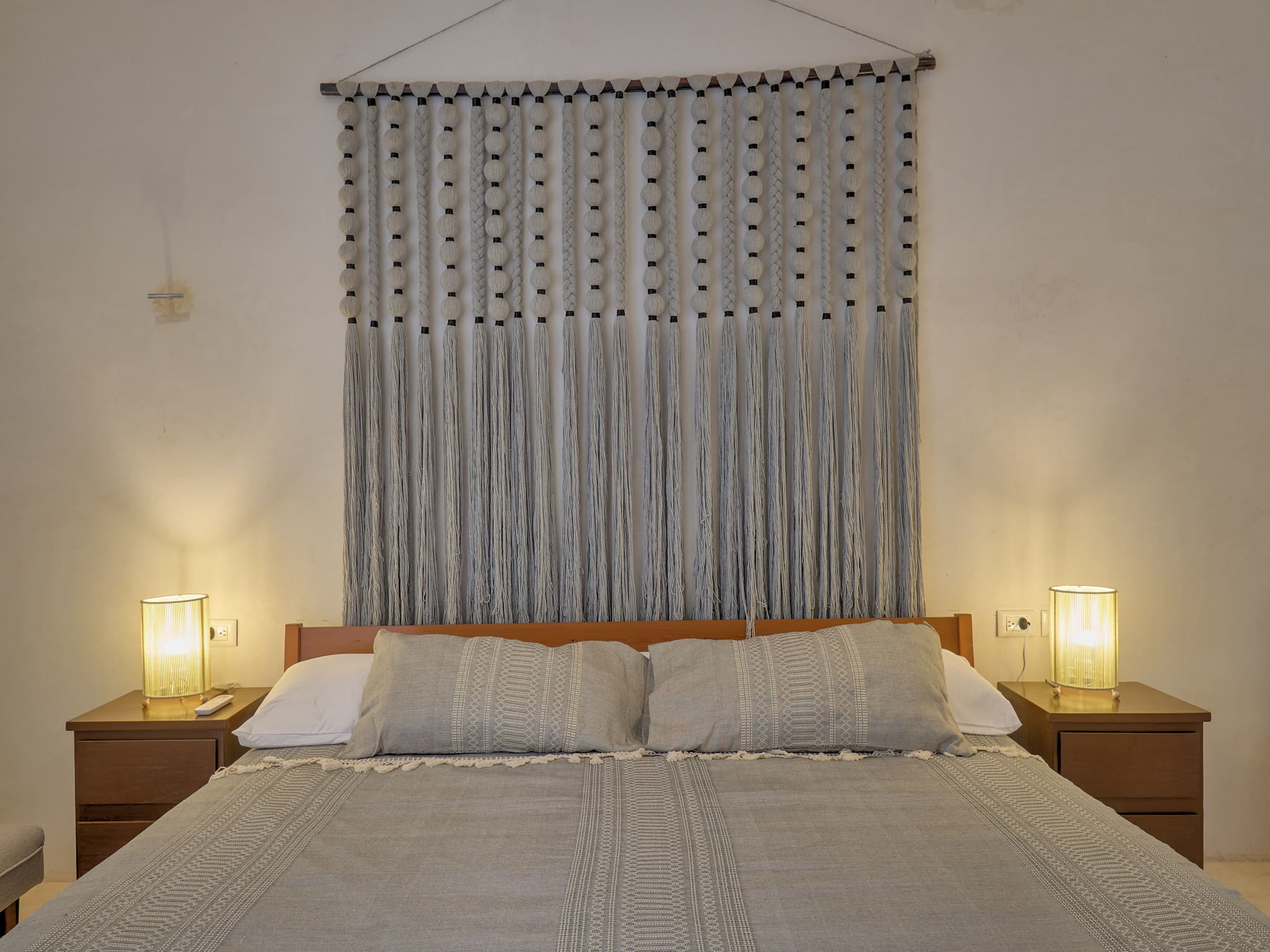 Cozy bedroom with a beige bed and decorative macramé wall hanging.