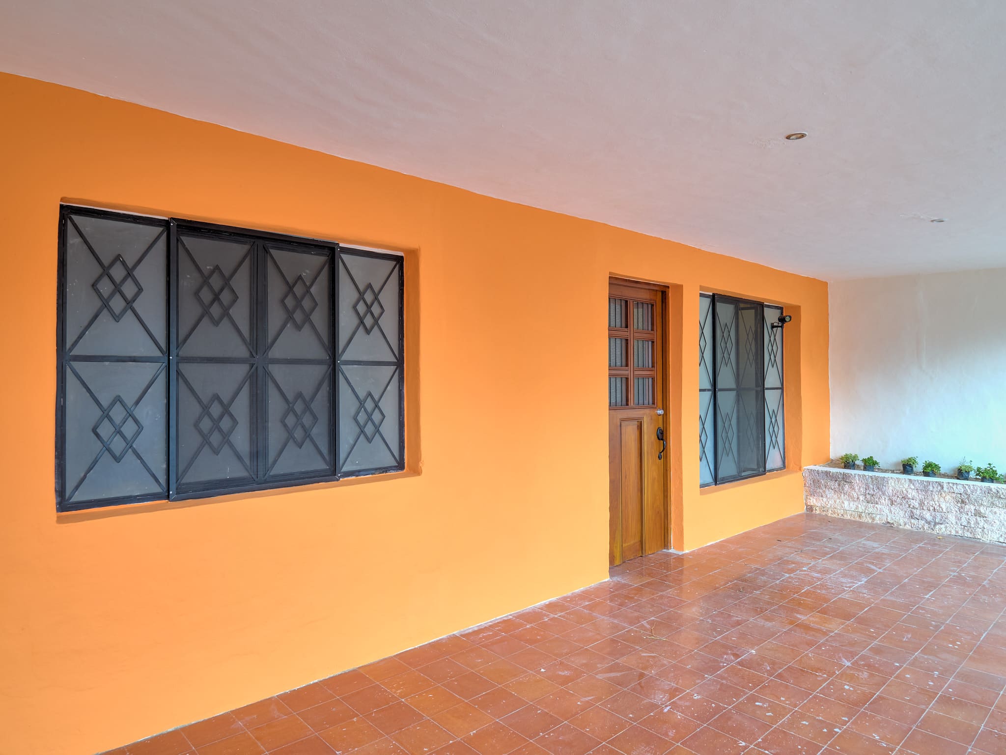 Orange-painted wall with windows and a wooden door on a porch.