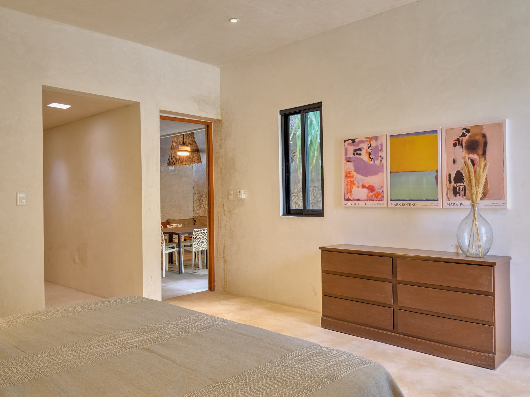 Minimalist bedroom with wooden dresser and colorful artwork on the wall.