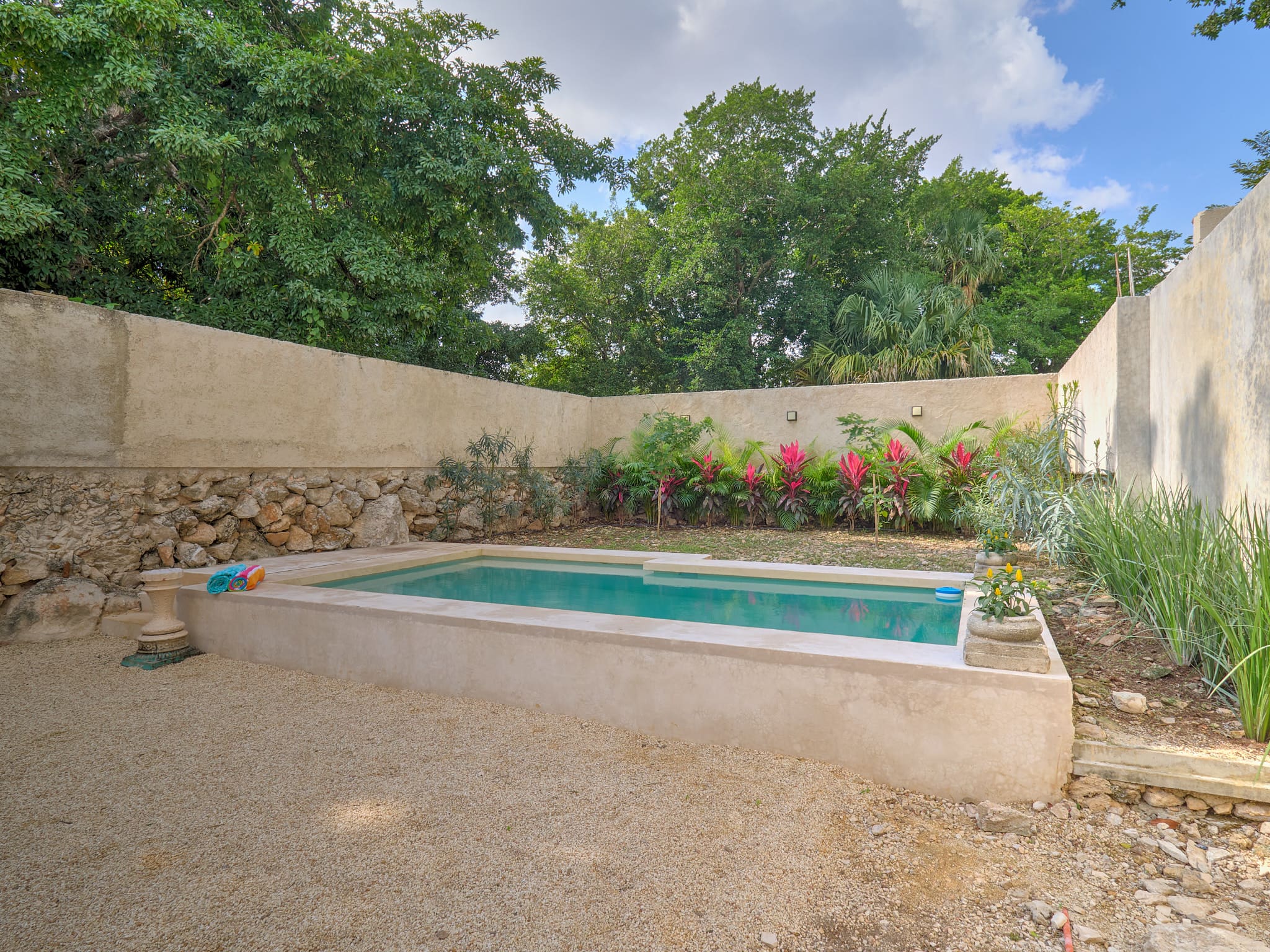 A serene backyard pool surrounded by stone walls and greenery.