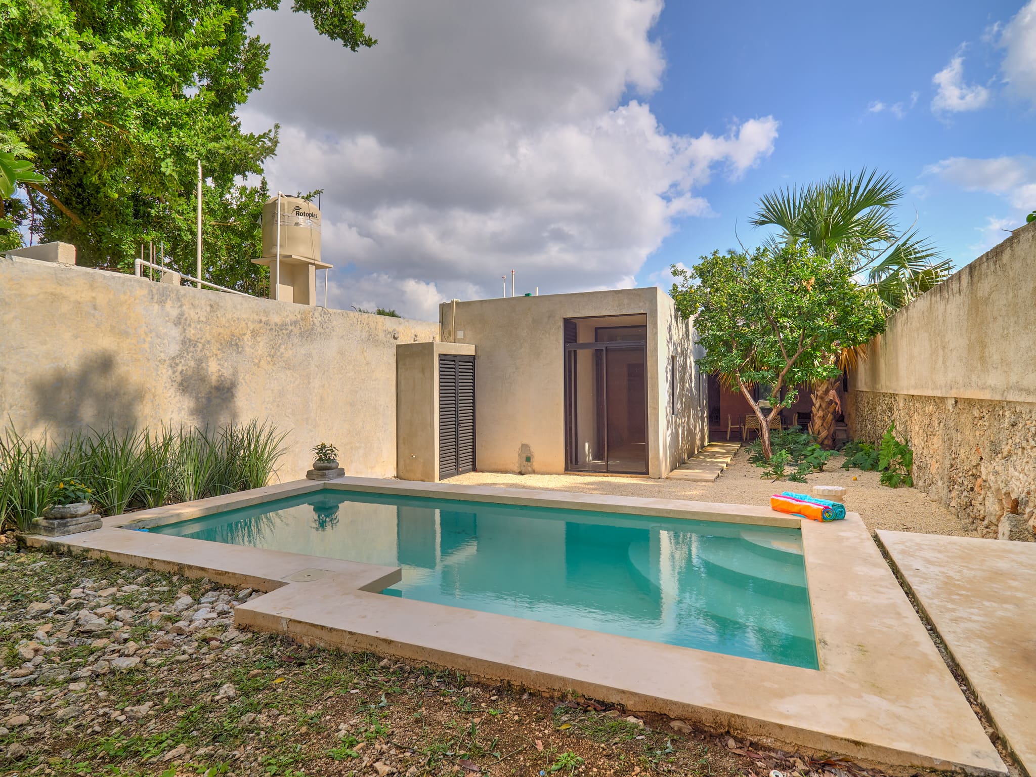 Tranquil backyard with a small pool and rustic stone walls under a partly cloudy sky.
