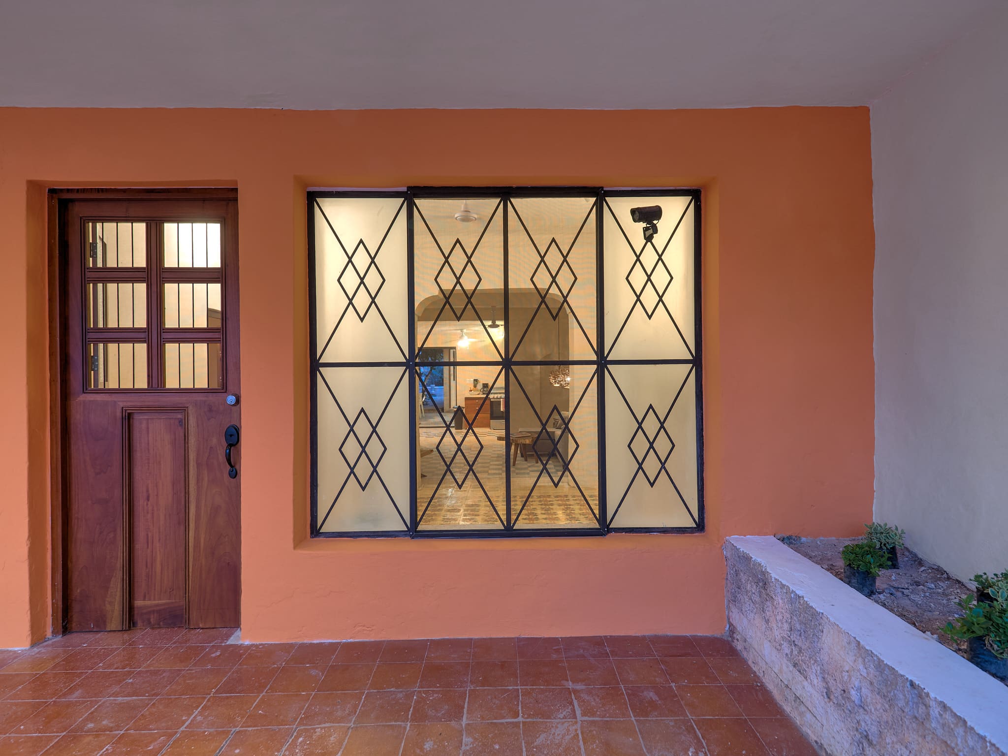 A window with black metal bars on an orange wall beside a wooden door.