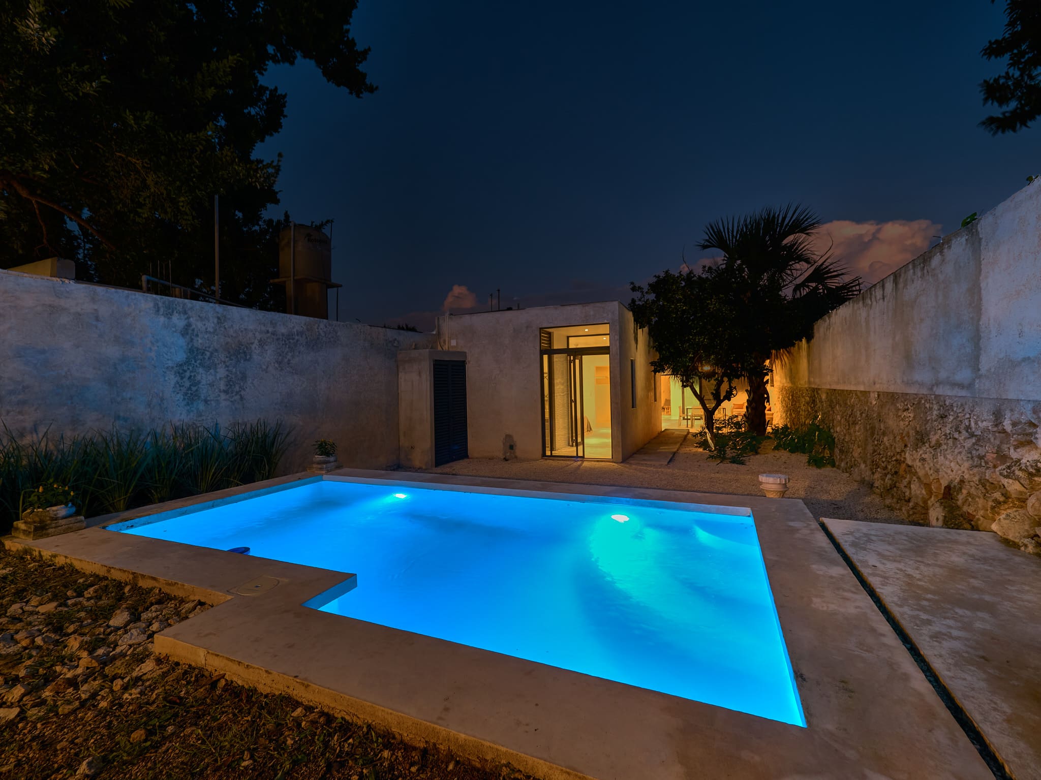 A modern backyard pool illuminated at night with blue lights.