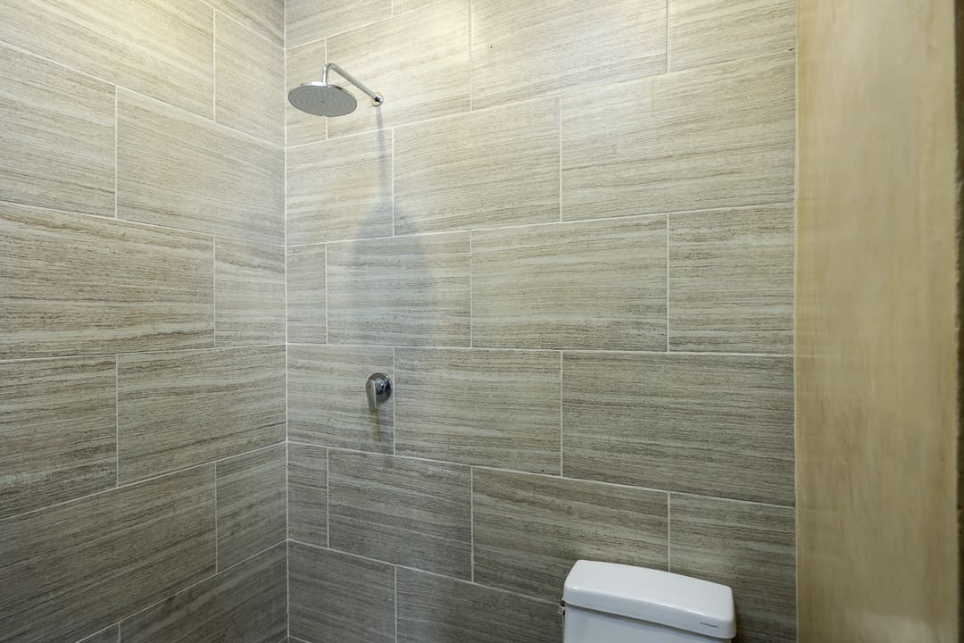 Minimalist bathroom shower area with beige tiles and a toilet.