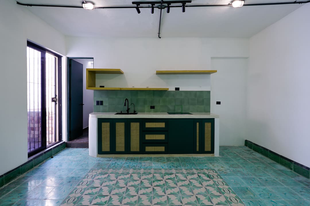 Modern kitchen with green tiles and black cabinetry under natural light.