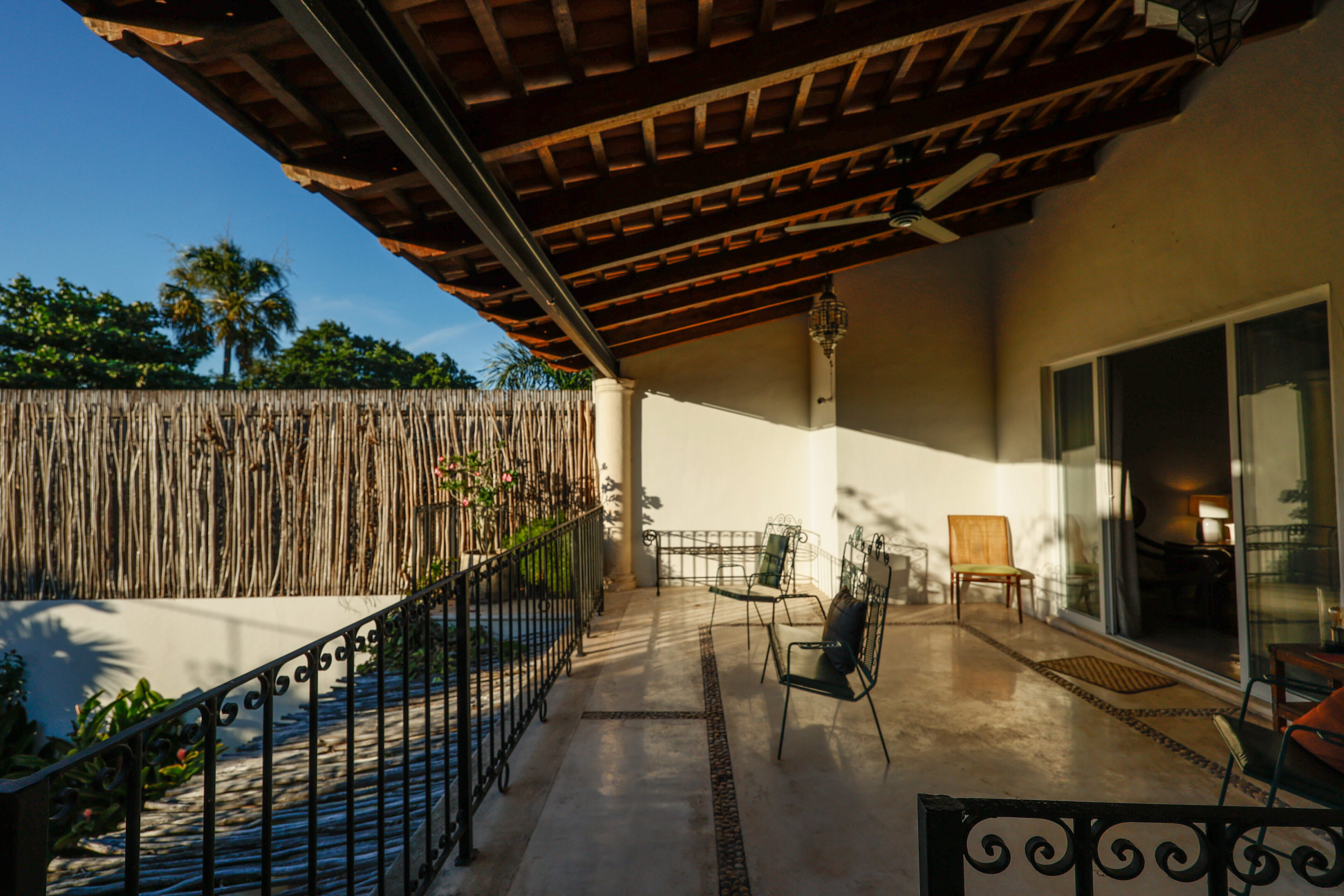 Sunny patio with metal chairs and a wooden roof.