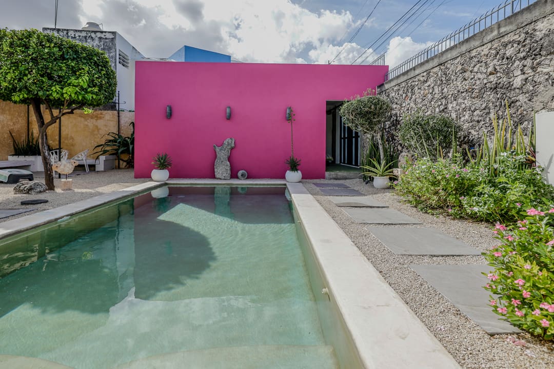 Modern backyard pool with a vibrant pink wall and sculptures.