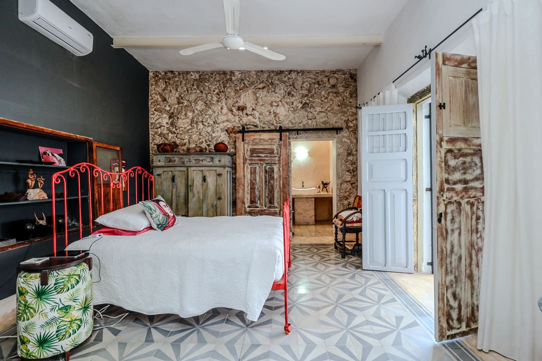 Cozy bedroom with rustic stone wall and vintage red metal bed frame.