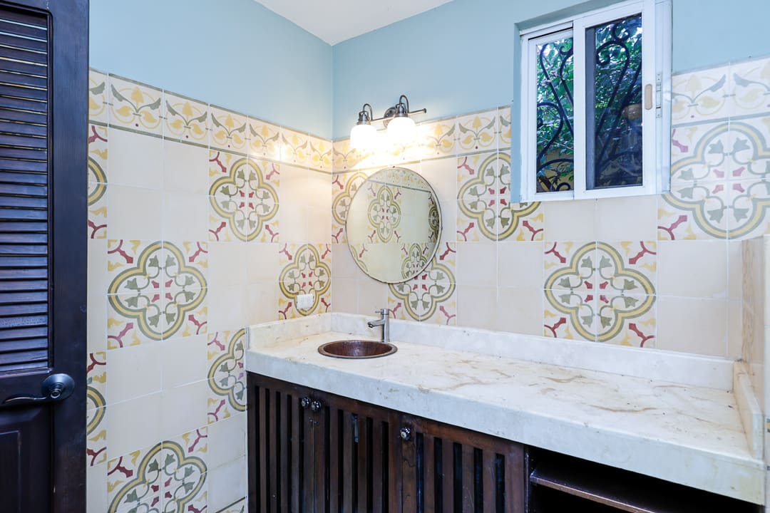 Vintage bathroom with ornate tiled walls and a round mirror.