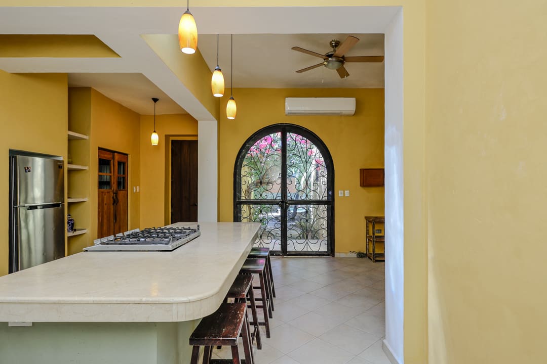 Modern kitchen with yellow walls and bar stools by a large arched window.
