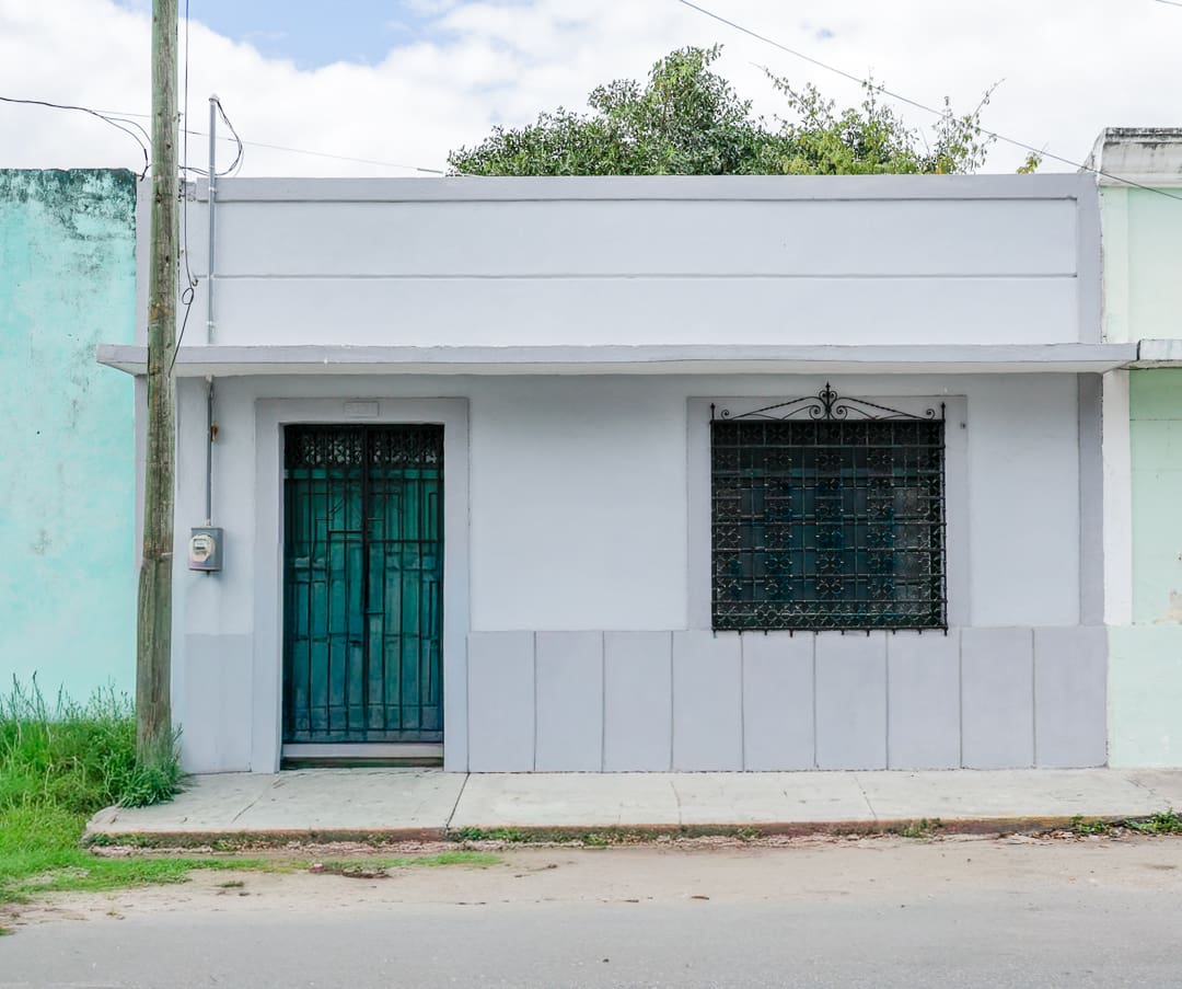 Simple single-story house with teal door and barred window.