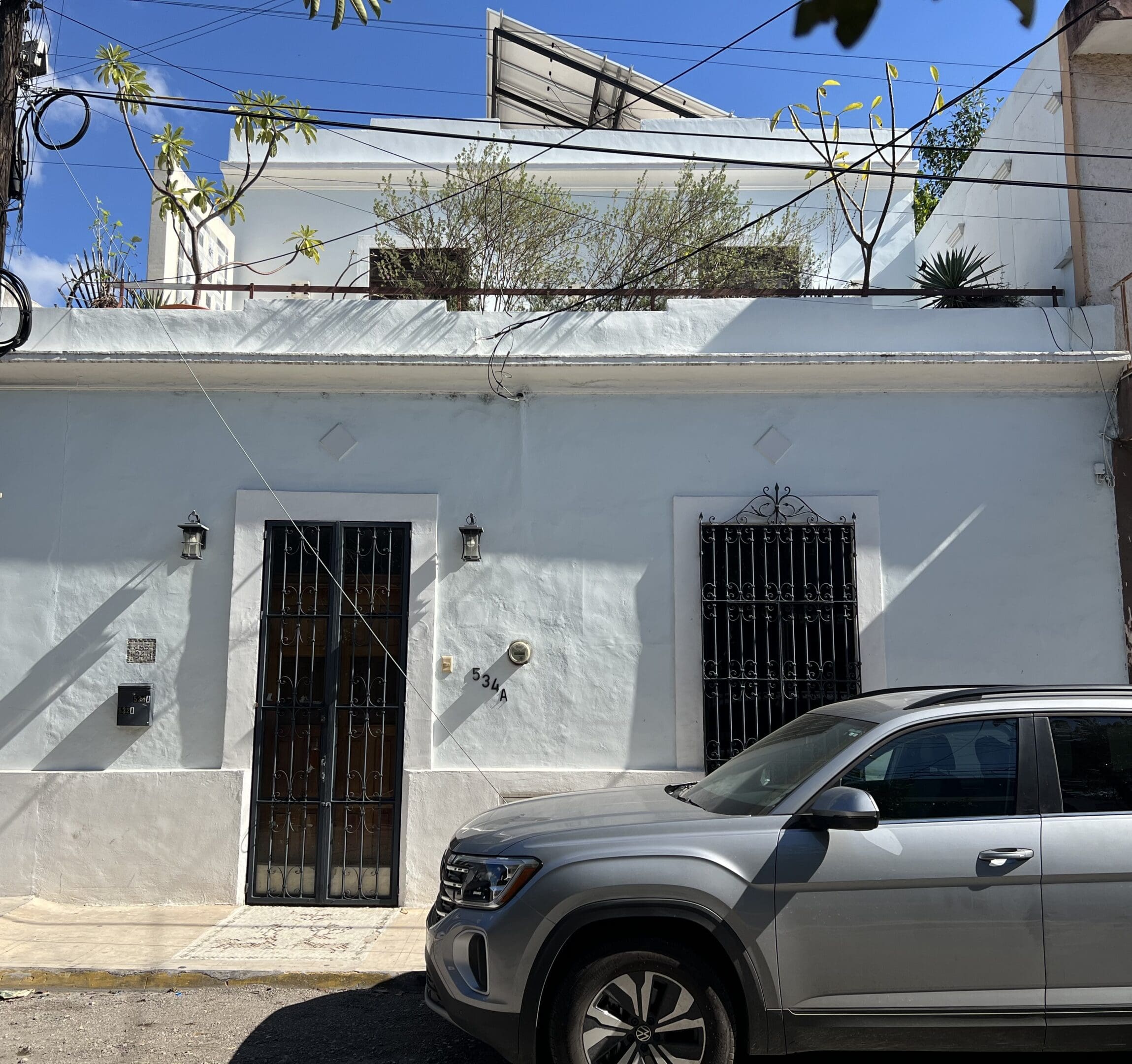White building with barred windows and a parked gray car in front.