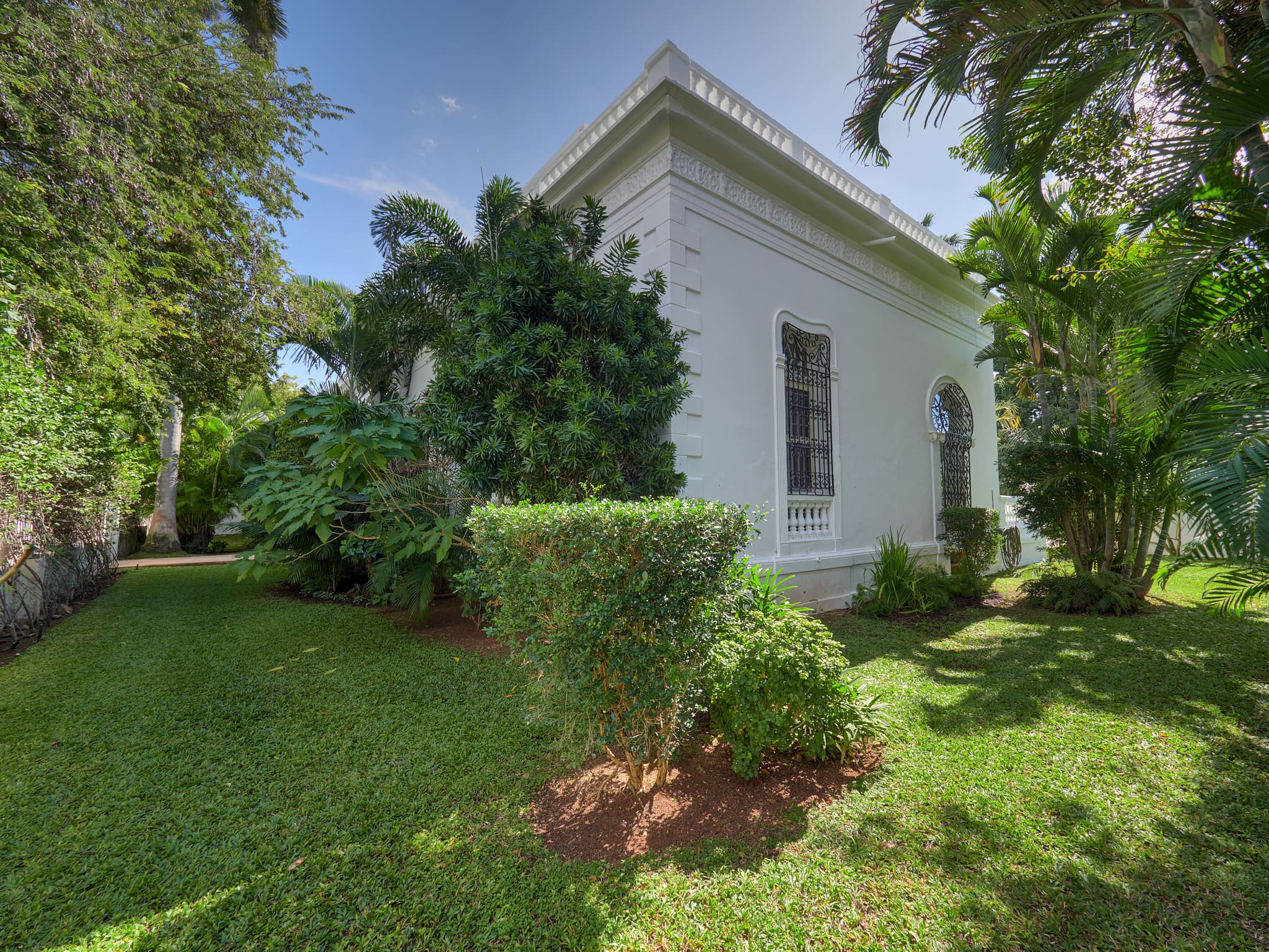 A white house surrounded by lush greenery and trees on a sunny day.