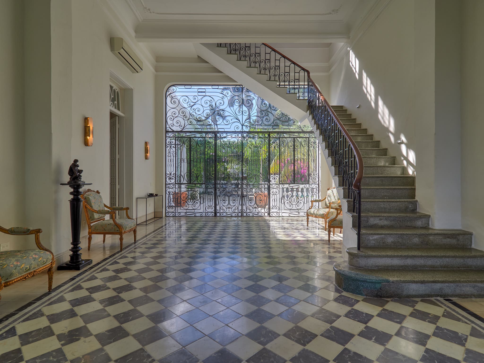 Elegant foyer with checkered floor and curved staircase opening to garden.