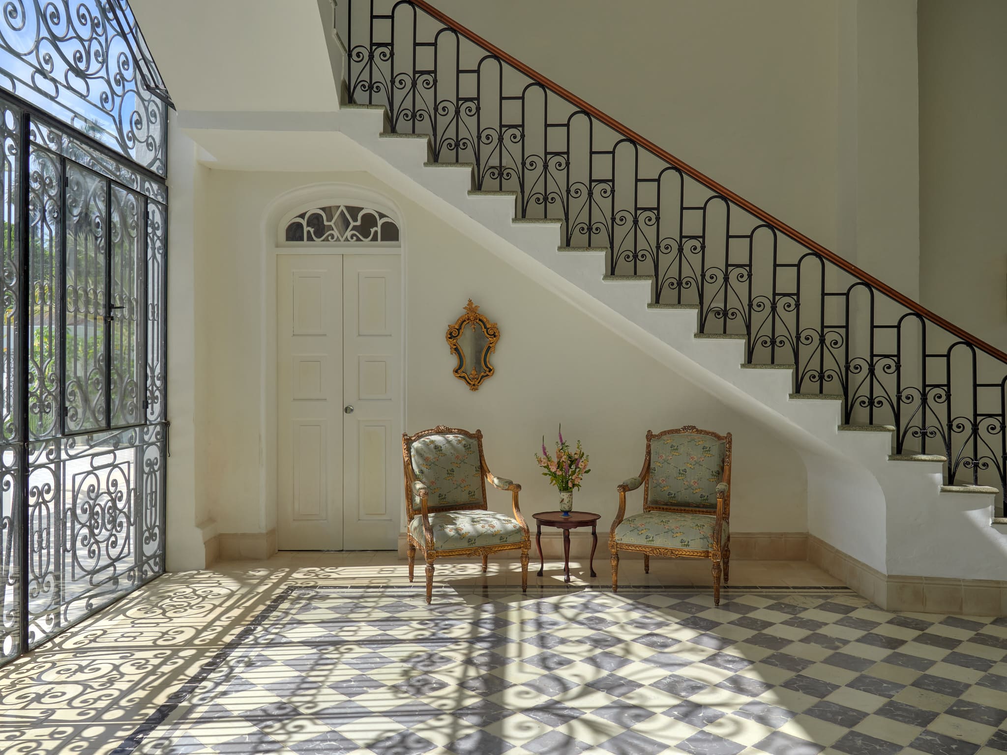Elegant vintage chairs and a table under a staircase with patterned floor tiles.