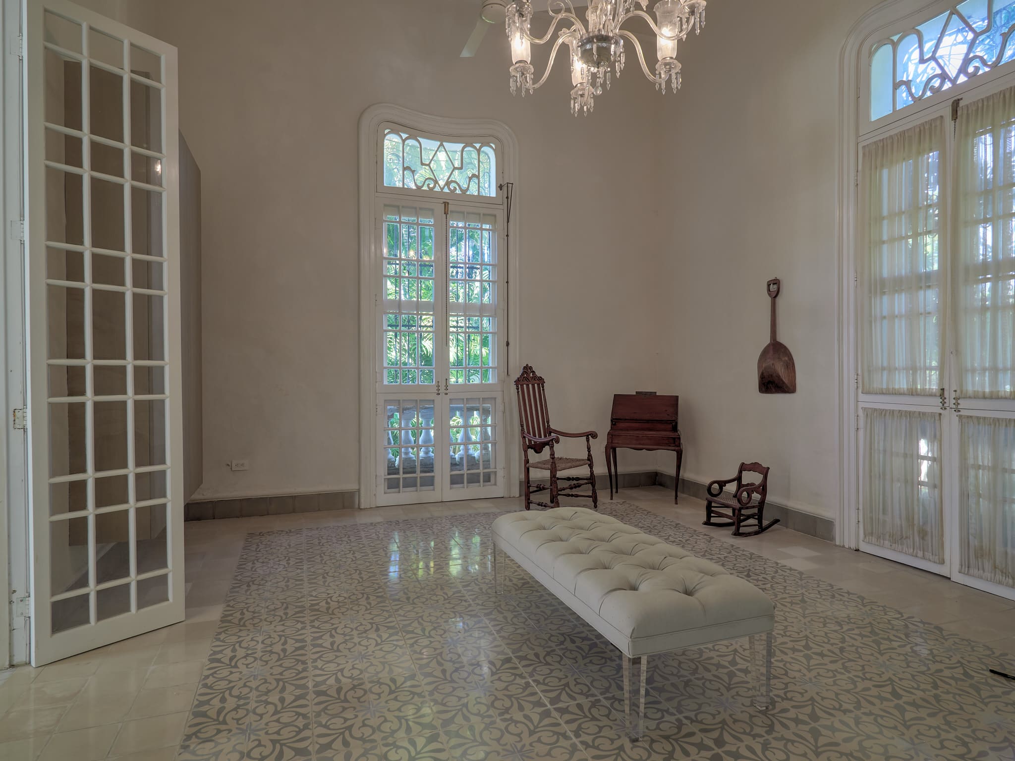 A serene, minimally furnished room with large windows and ornate chandelier.
