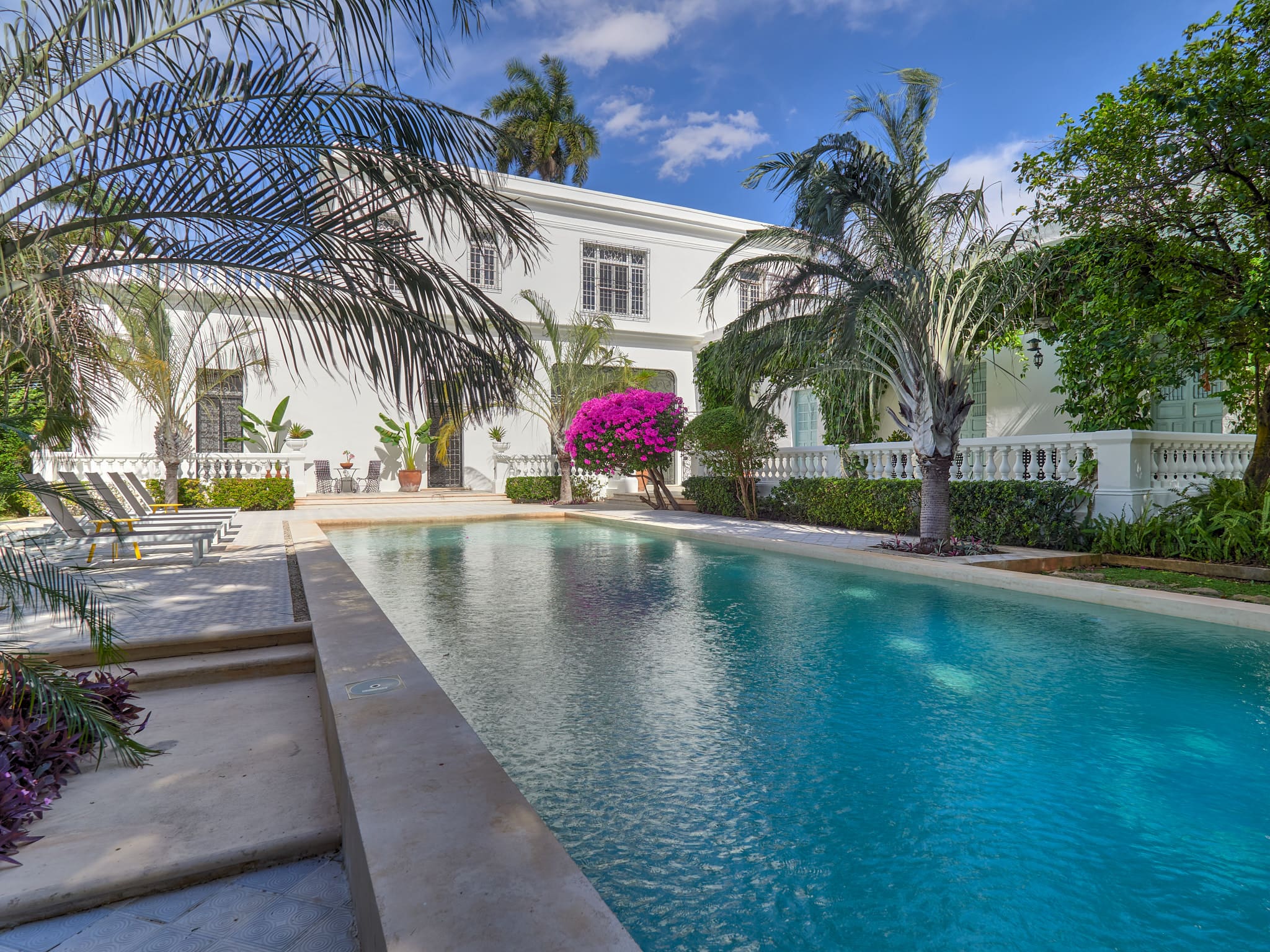 Elegant white villa with a serene swimming pool and palm trees under a blue sky.