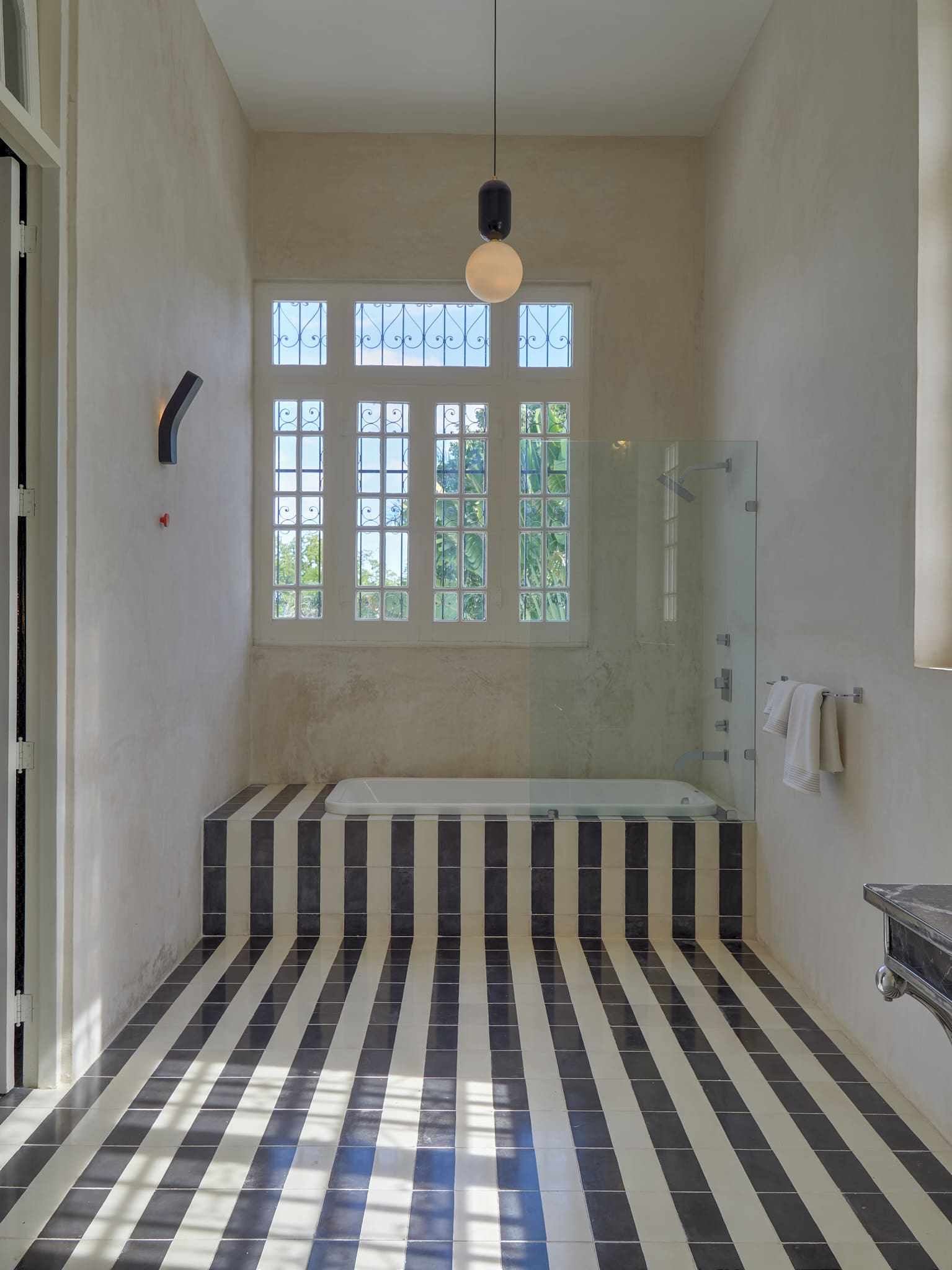Modern bathroom with striped floor and glass shower enclosure under large window.