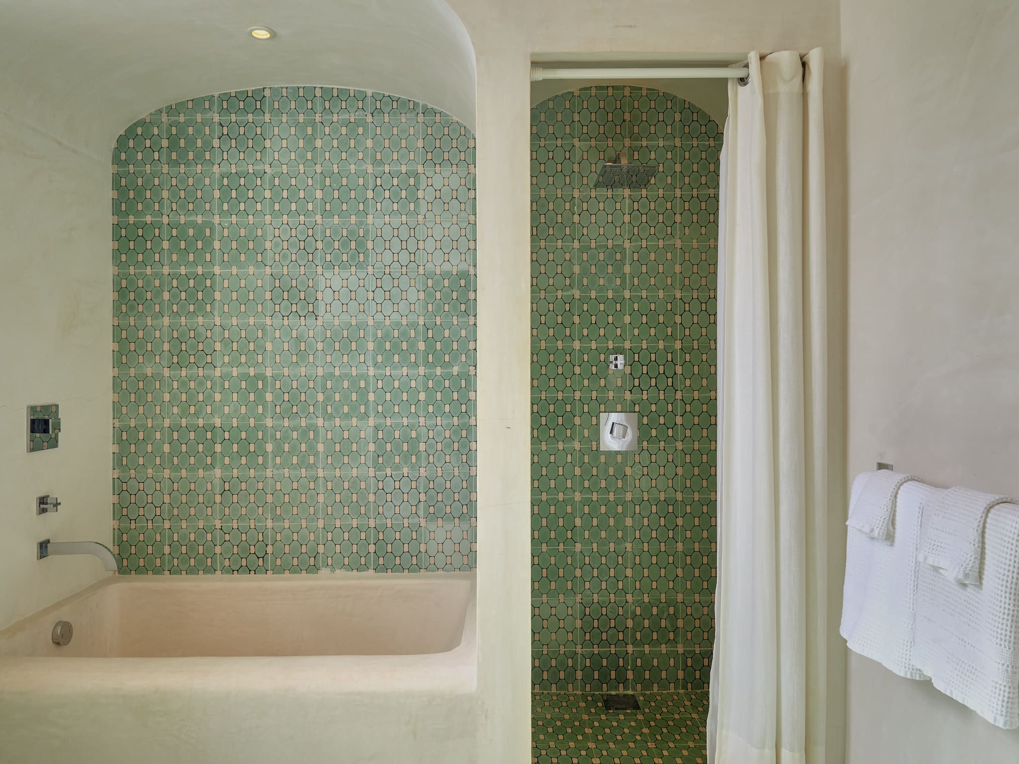 A bathroom shower with green patterned tiles and a curtain.