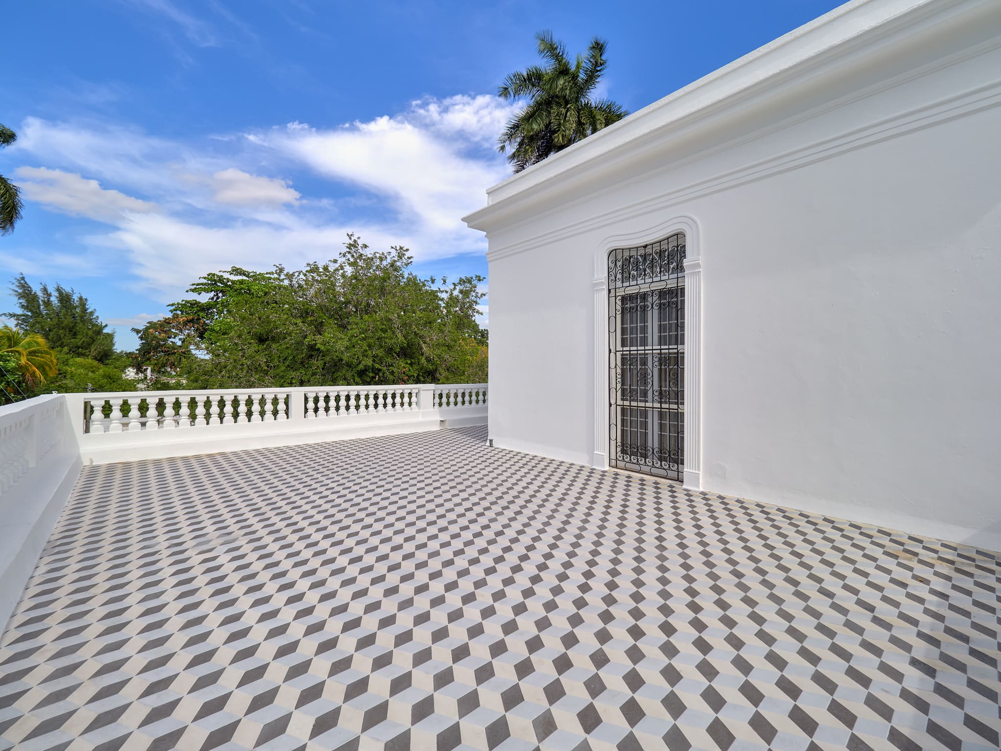Spacious terrace with patterned tile flooring and bright white walls under a blue sky.