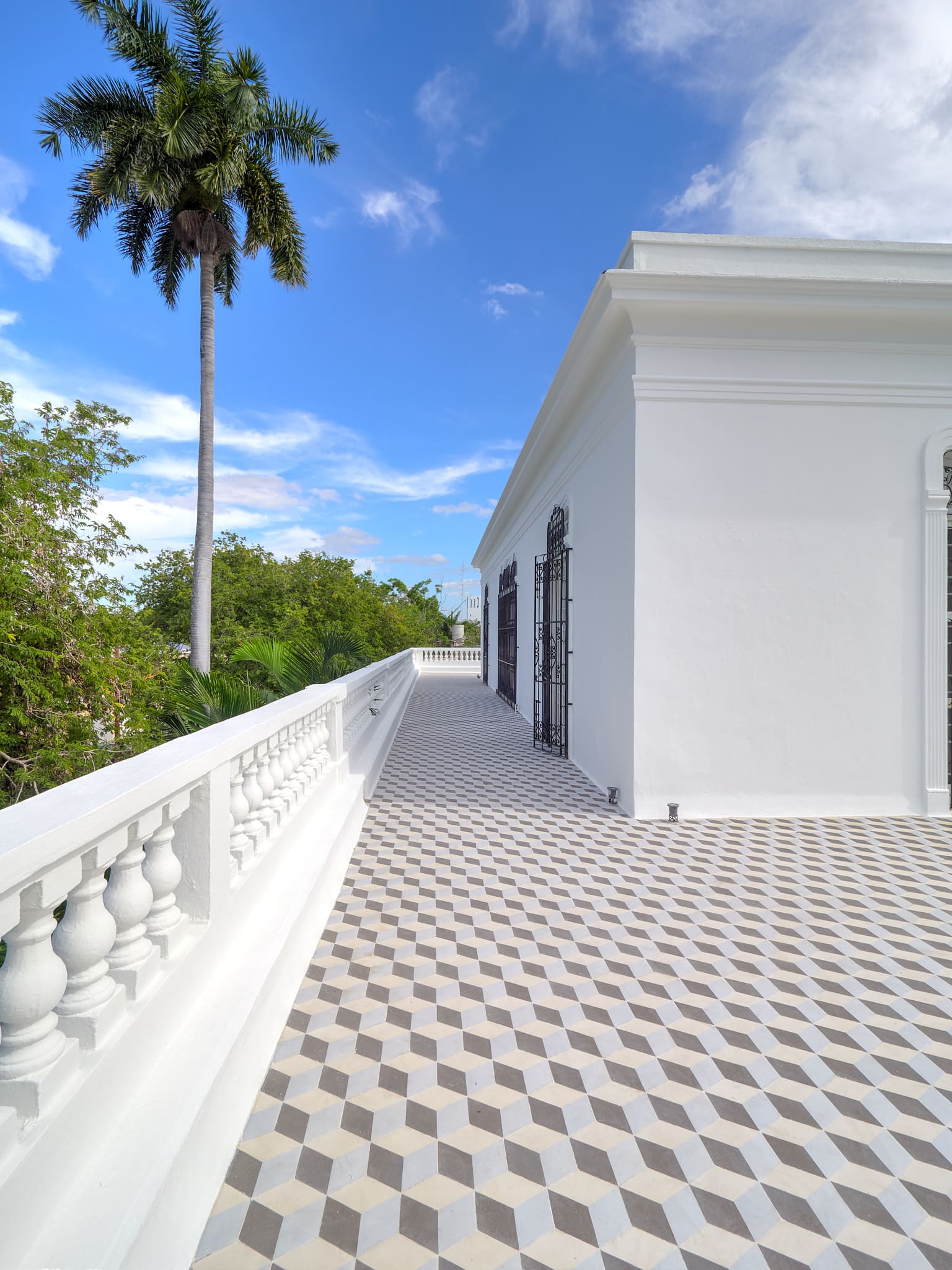 White balcony with patterned tile floor and palm trees under a blue sky.