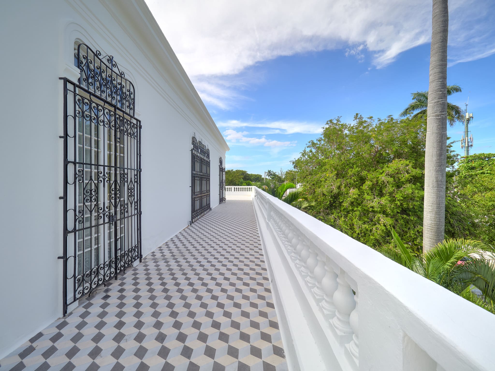 Bright balcony with patterned floor tiles and white railing overlooking green trees.