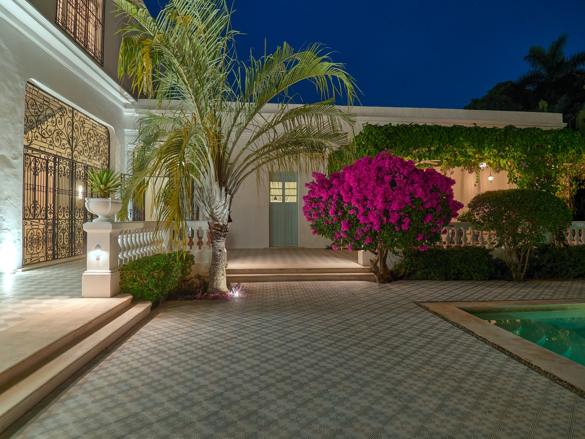 Elegant courtyard with vibrant pink flowers and warm lighting at night.