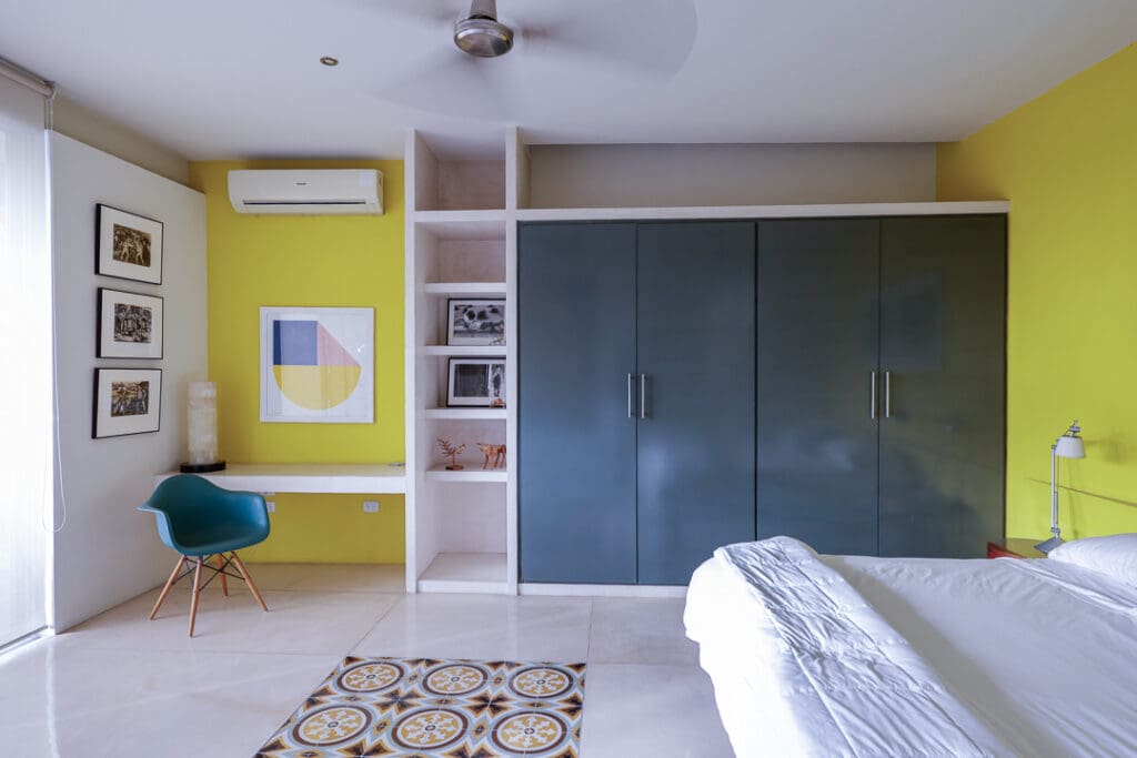 Modern bedroom with green wardrobe and yellow accent wall.