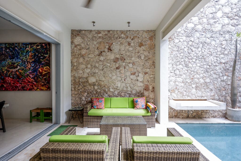 Cozy outdoor seating area with green cushions and rustic stone wall.