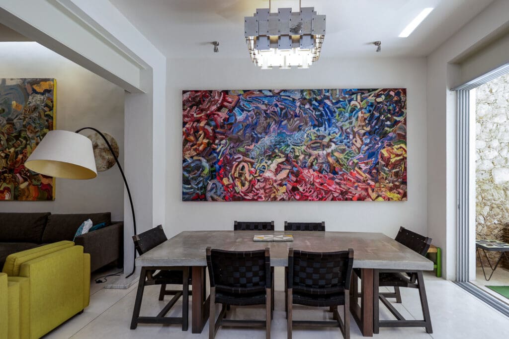 Modern dining area with a large colorful abstract painting and black chairs.