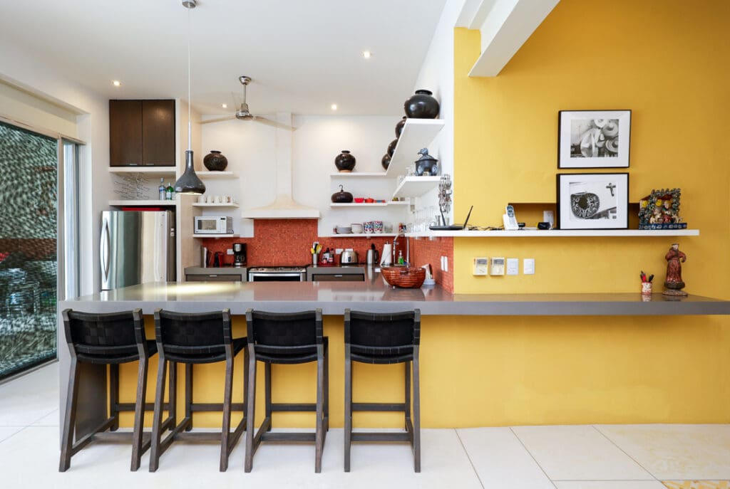 Modern kitchen with a bright yellow accent wall and black bar stools.