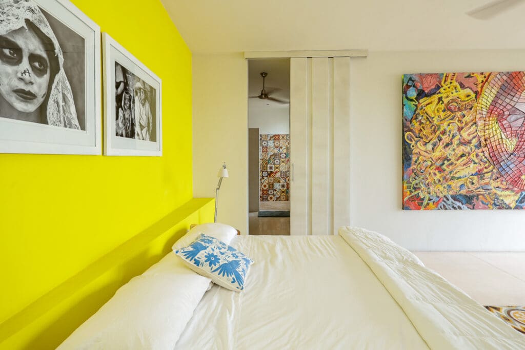 Bright bedroom with yellow walls and colorful artwork.