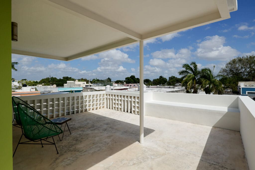 Sunny rooftop patio with white railings and a table set under a covered area.