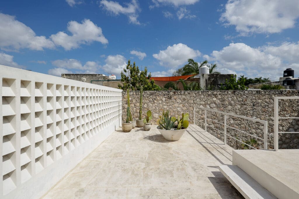 Bright outdoor terrace with white walls and potted plants under a blue sky.