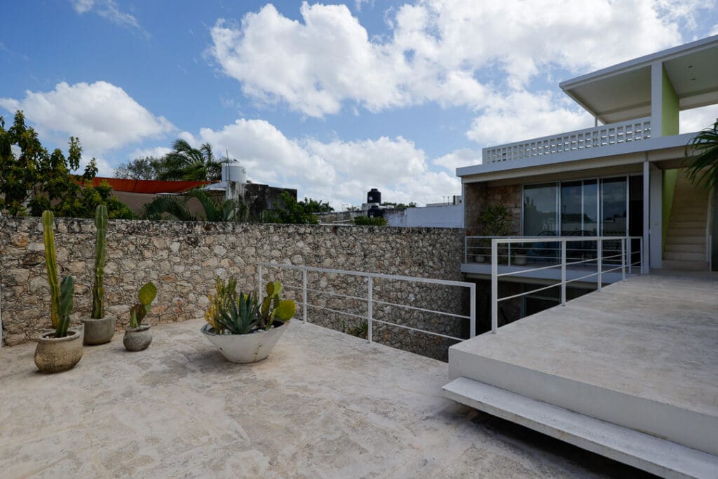 Modern outdoor terrace with stone wall and plants under a partly cloudy sky.