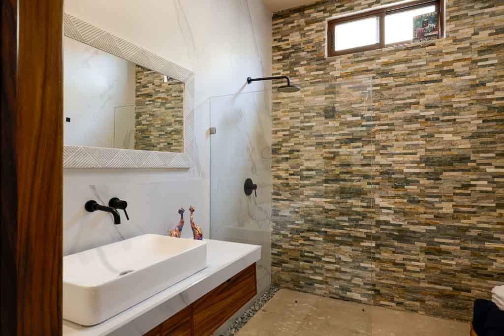 Modern bathroom with stone accent wall and glass shower.
