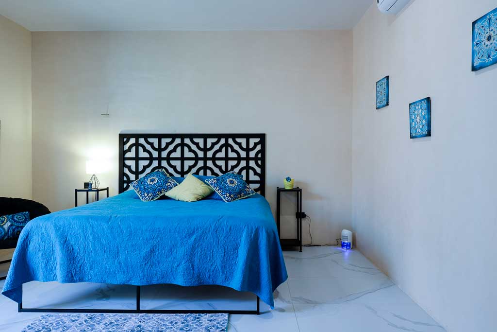 A bedroom with a blue bedspread and decorative headboard.